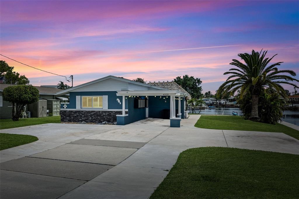 A blue house with a stone base and a covered carport sits near a canal — 4320 FLORAMAR TERRACE, NEW PORT RICHEY, FL