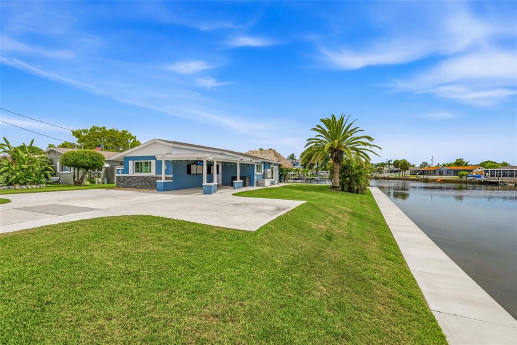 A blue house with a concrete driveway sits on a grassy lot beside a canal — 4320 FLORAMAR TERRACE, NEW PORT RICHEY, FL