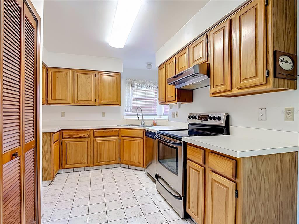 A kitchen with light wood cabinets, white countertops, stainless steel appliances, and white tile flooring — 4130 BERGAMONT COURT, KISSIMMEE, FL