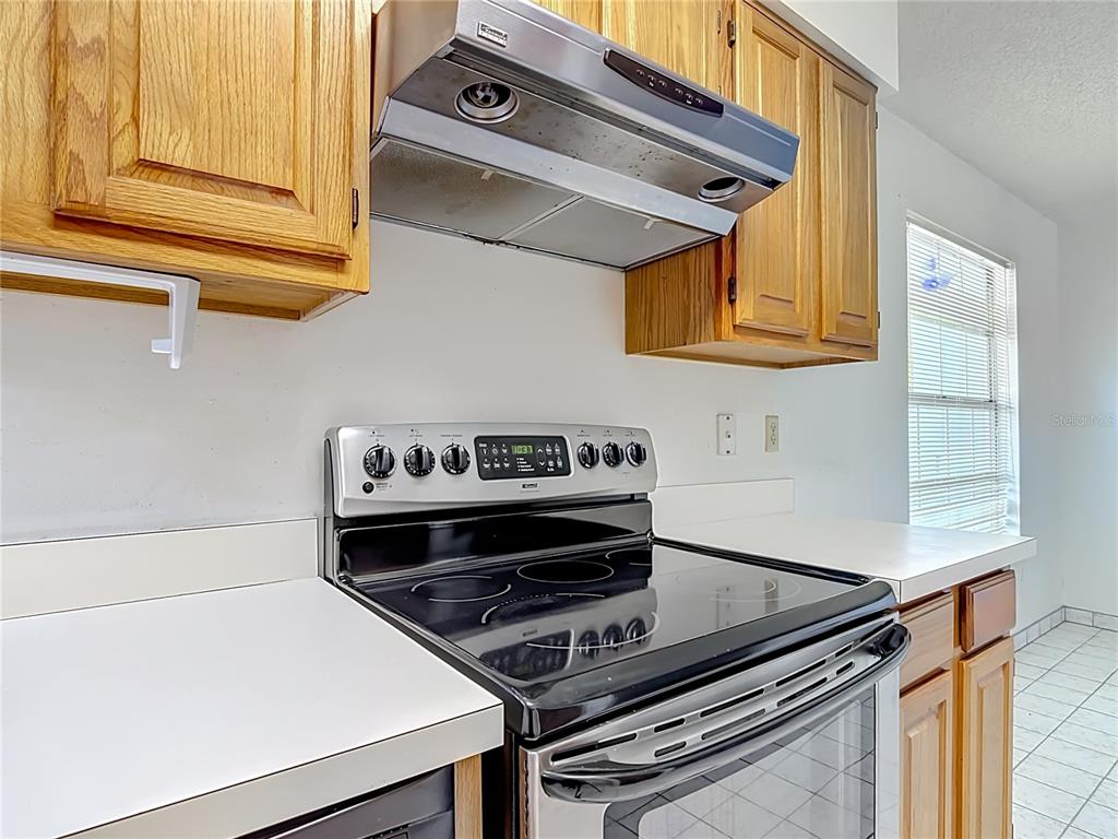 A kitchen features wooden cabinets, a stainless steel range hood, and a black glass-top stove — 4130 BERGAMONT COURT, KISSIMMEE, FL