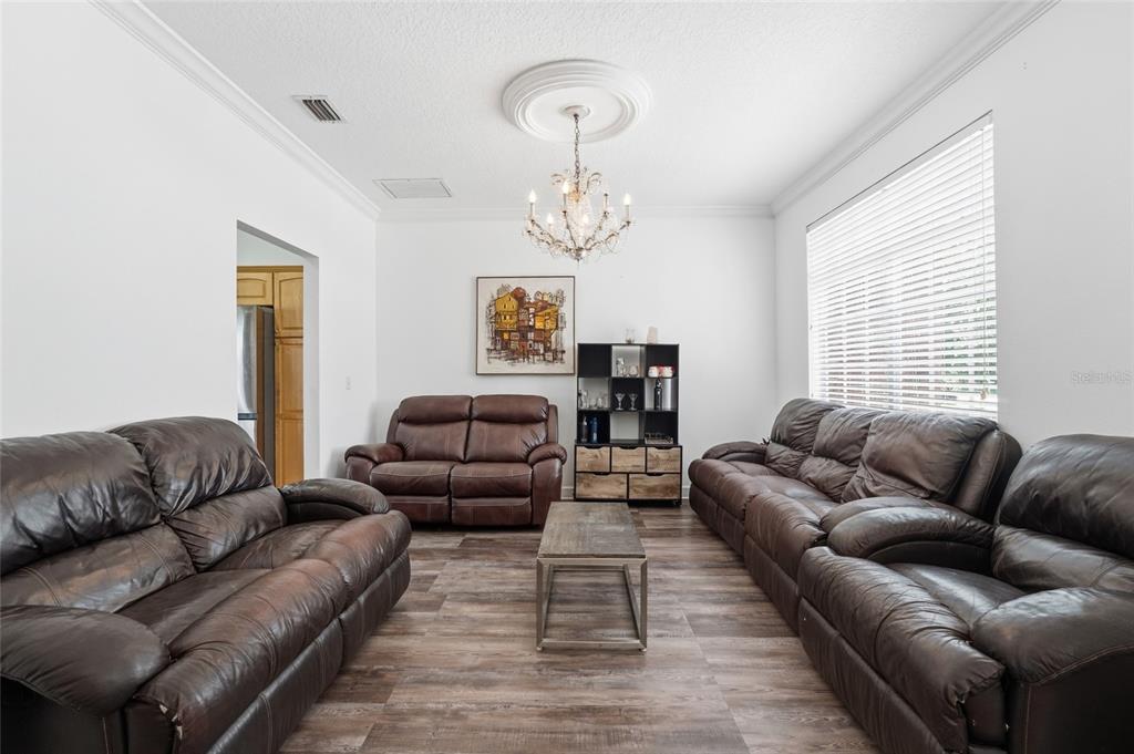 A living room features three brown leather sofas, a coffee table, and a crystal chandelier — 9137 DOLLANGER COURT, ORLANDO, FL