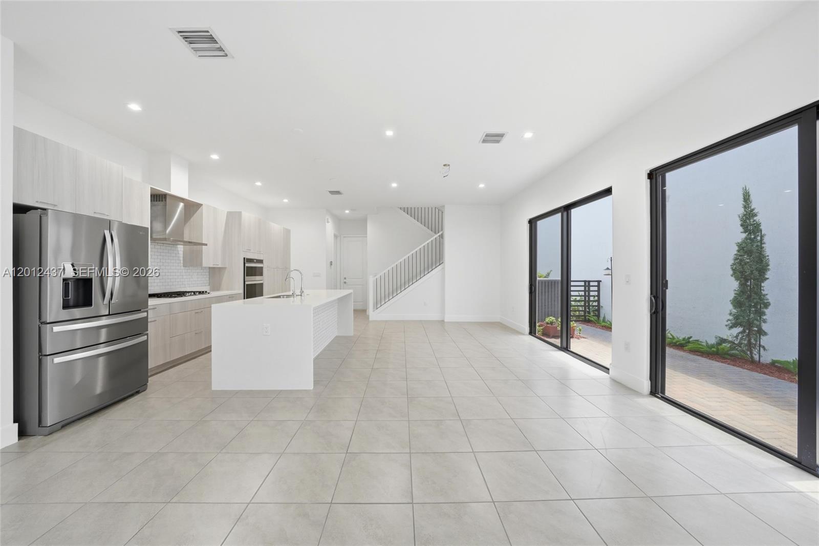 A modern kitchen with a white island and stainless steel appliances opens to a patio — 4356 NW 80th Ave, Doral FL 33166, DORAL, FL