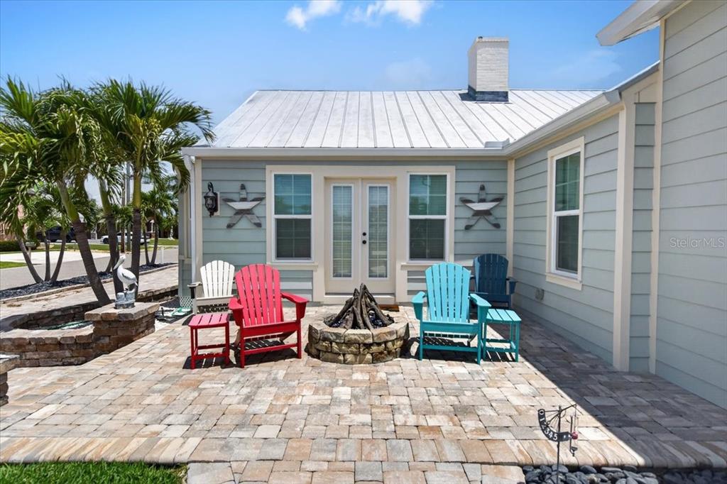 A stone patio features a fire pit and colorful Adirondack chairs in front of a house — 216 SUNRISE DRIVE, NOKOMIS, FL