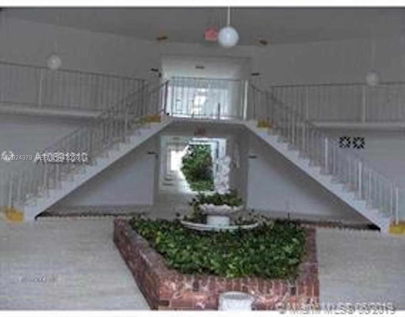A lobby features a central brick planter with greenery, a fountain, and symmetrical staircases — 6505 Winfield Blvd # 3, Margate FL 33063, MARGATE, FL