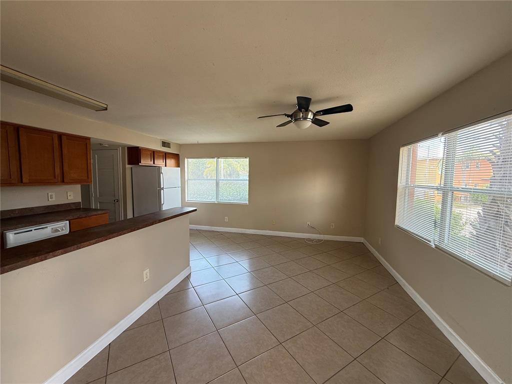 A kitchen with wood cabinets and a breakfast bar opens into a tiled living area — 117 N EVERGREEN AVENUE UNIT 105, CLEARWATER, FL