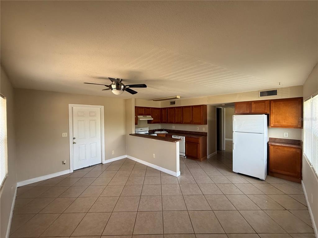 A kitchen with wood cabinets and tile flooring opens into a living area — 117 N EVERGREEN AVENUE UNIT 105, CLEARWATER, FL