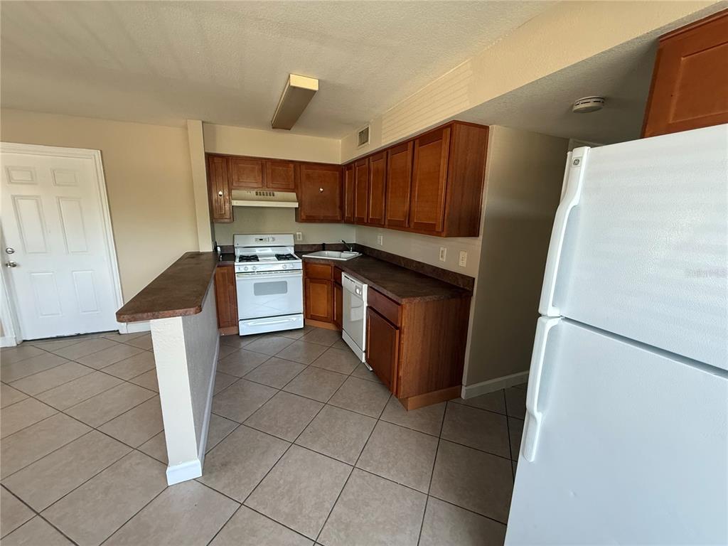 A kitchen features wood cabinets, dark countertops, white appliances, and light-colored tile flooring — 117 N EVERGREEN AVENUE UNIT 105, CLEARWATER, FL