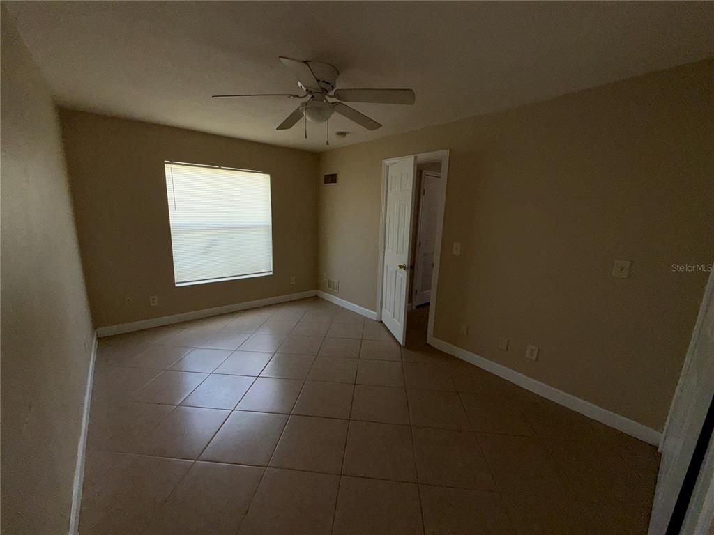 An empty room features beige walls, tile flooring, a ceiling fan, and a window — 117 N EVERGREEN AVENUE UNIT 105, CLEARWATER, FL