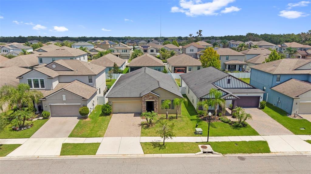 An aerial view shows three suburban houses with driveways and lawns along a paved street — 13244 SATIN LILY DRIVE, RIVERVIEW, FL