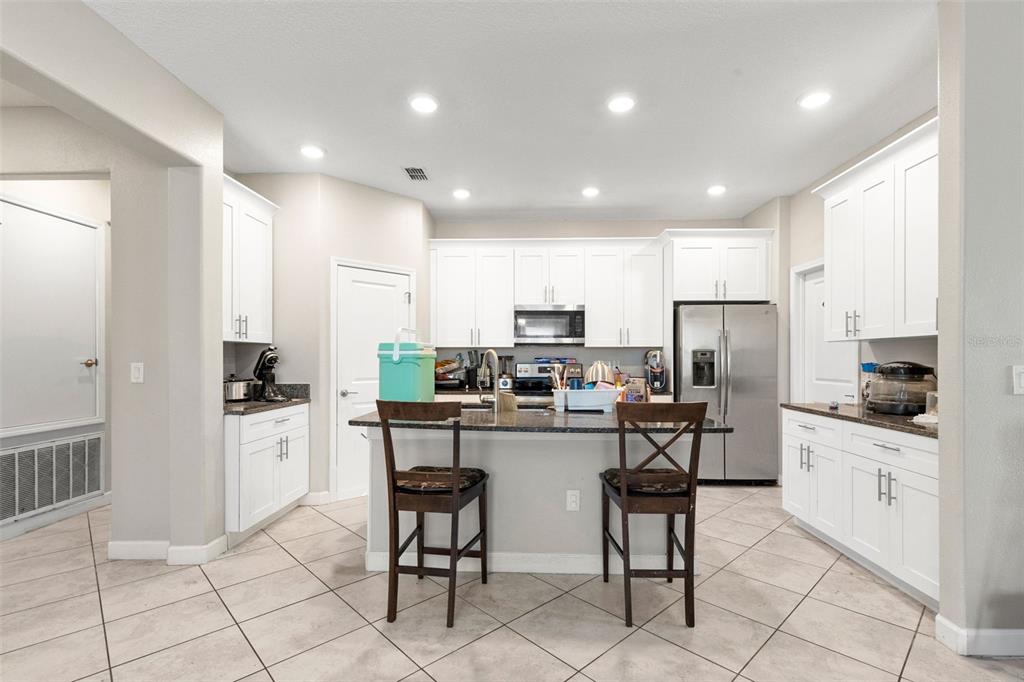 A kitchen features white cabinets, a dark granite island with two chairs, and tile flooring — 13244 SATIN LILY DRIVE, RIVERVIEW, FL