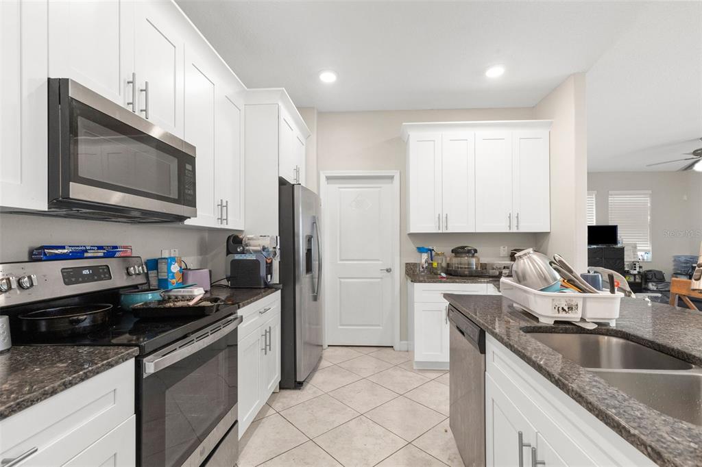 A kitchen features white cabinets, stainless steel appliances, dark granite countertops, and tile flooring — 13244 SATIN LILY DRIVE, RIVERVIEW, FL