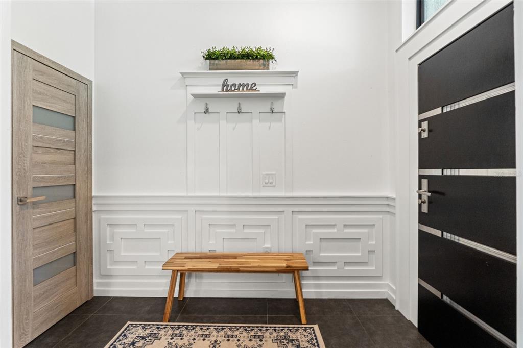 An entryway features a wooden bench, wall molding, coat hooks, and a modern front door — 24405 SUMMER WIND COURT, LUTZ, FL