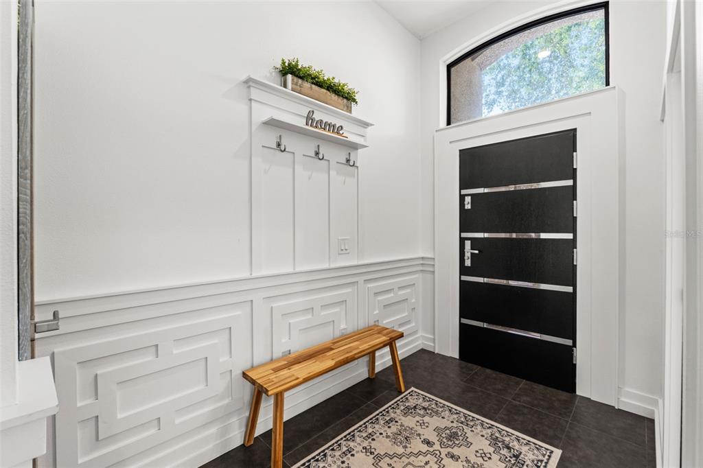 An entryway features a wooden bench, wall molding, a coat rack, and a modern black door — 24405 SUMMER WIND COURT, LUTZ, FL