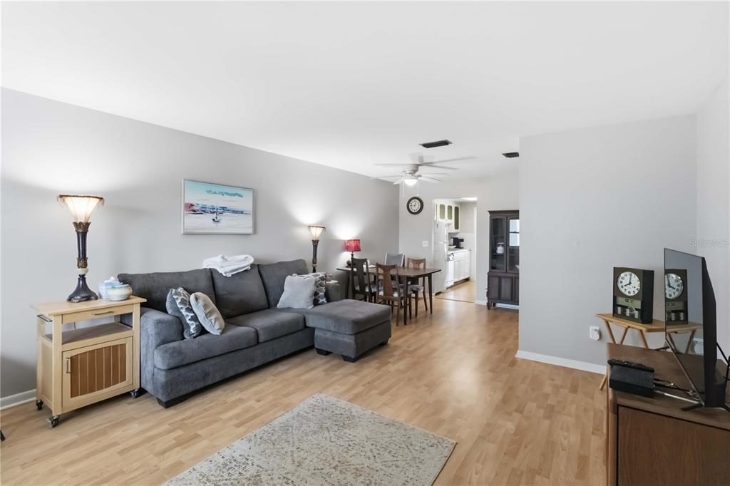 A living room features a grey sectional sofa, wood flooring, and an adjacent dining area — 6000 20TH STREET N UNIT 144, ST PETERSBURG, FL
