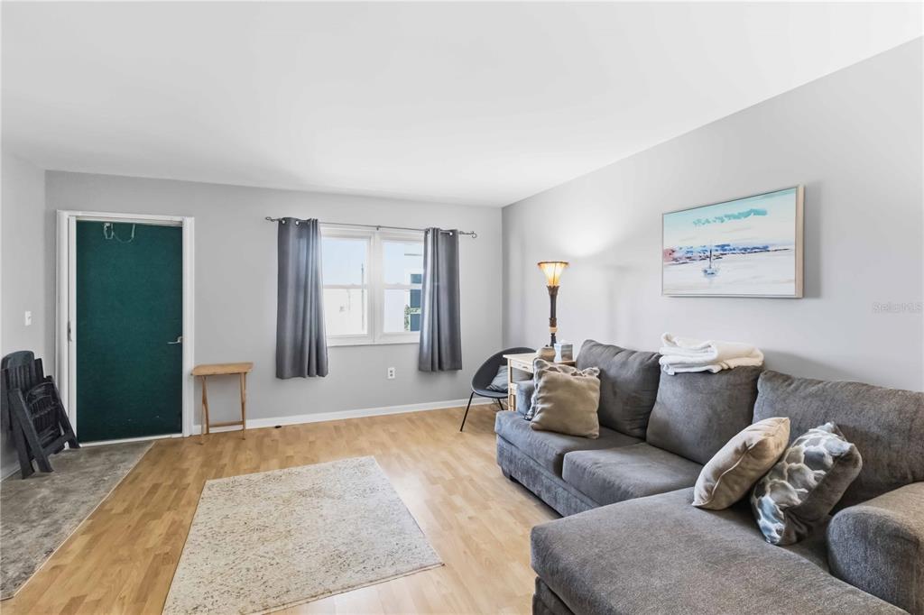 A living room features light wood flooring, a gray sectional sofa, and a dark door — 6000 20TH STREET N UNIT 144, ST PETERSBURG, FL