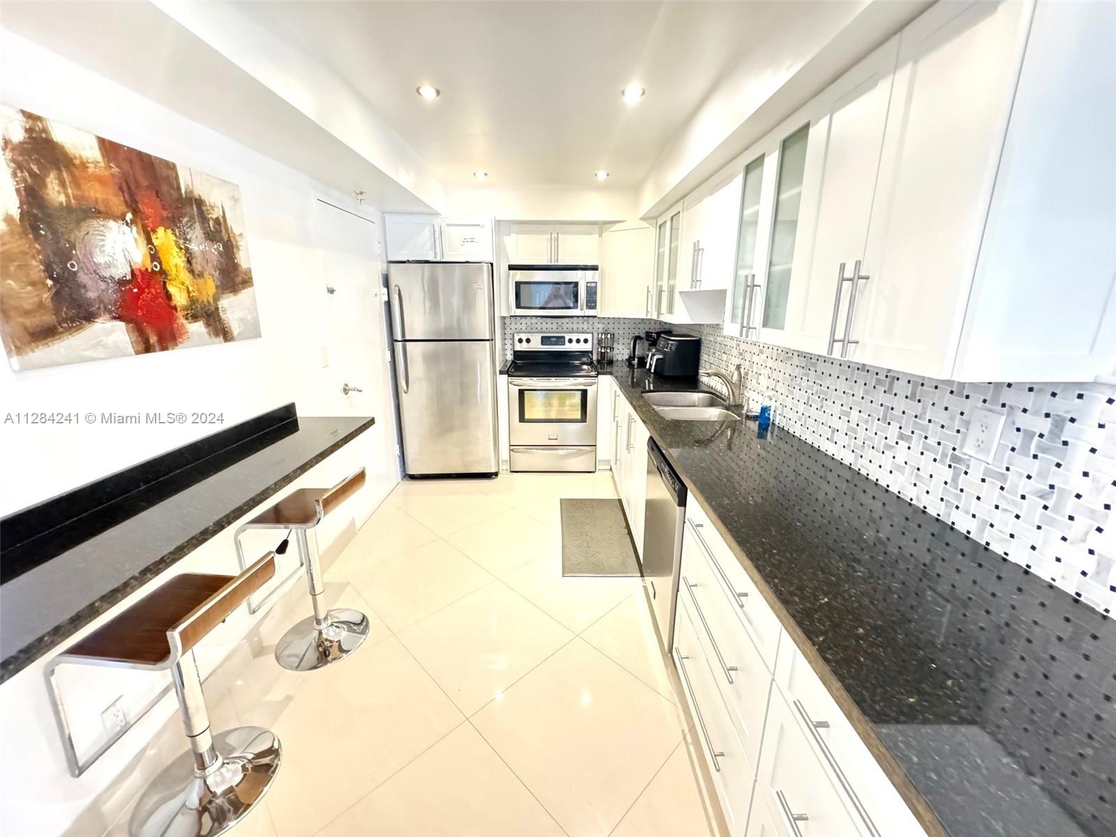 A modern kitchen features white cabinetry, black granite countertops, stainless steel appliances, and bar seating — 3901 S Ocean Dr # 8E, Hollywood FL 33019, HOLLYWOOD, FL