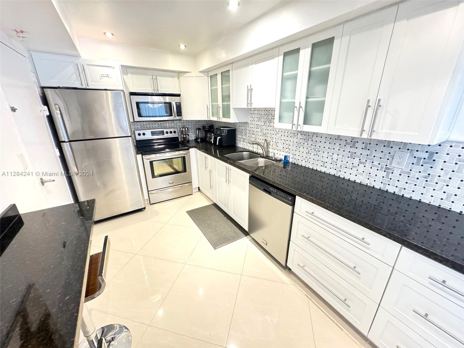 A kitchen features white cabinetry, stainless steel appliances, black granite countertops, and a tiled backsplash — 3901 S Ocean Dr # 8E, Hollywood FL 33019, HOLLYWOOD, FL