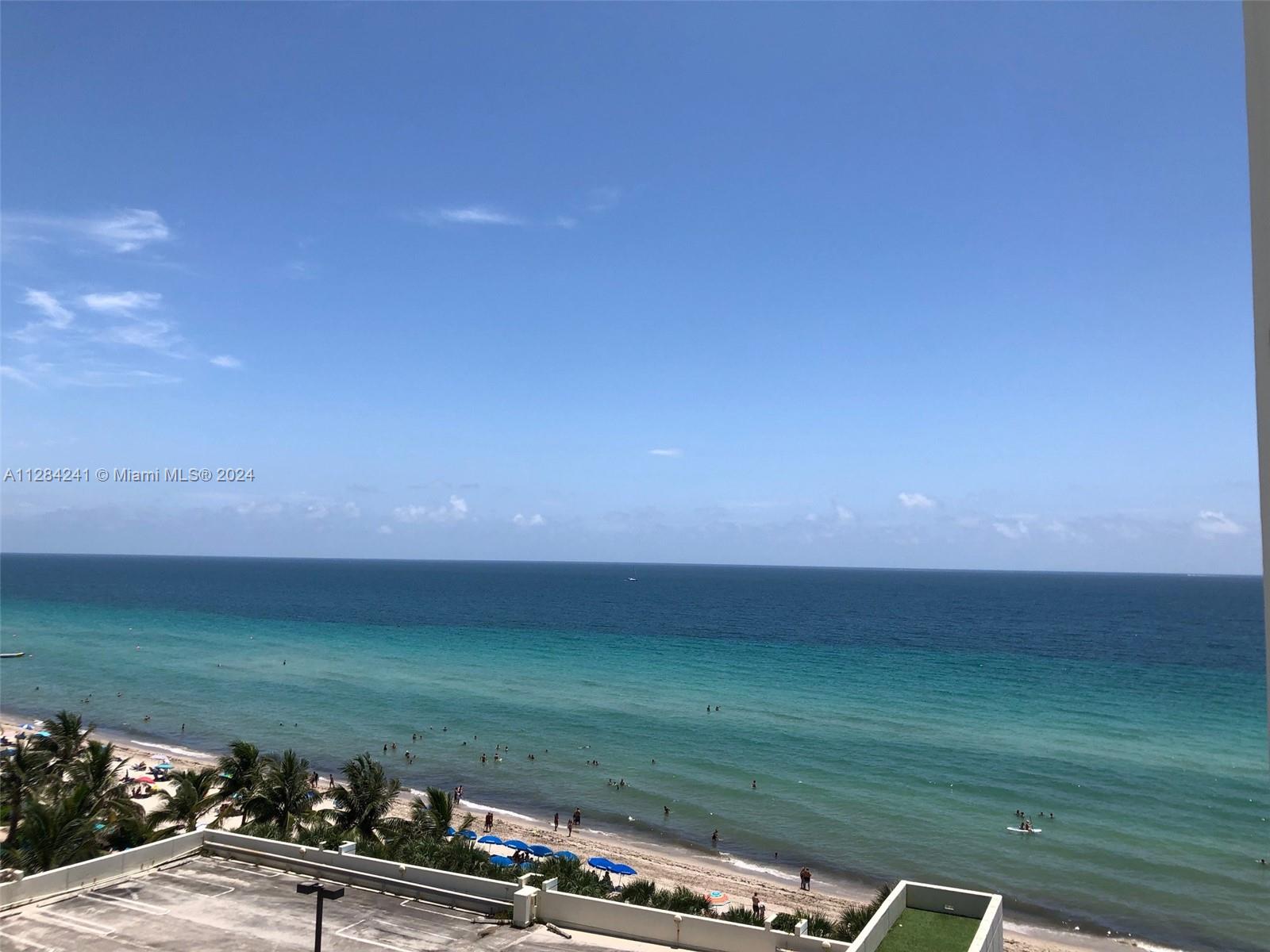 This high-angle view shows a beach with turquoise water, palm trees, and blue umbrellas — 3901 S Ocean Dr # 8E, Hollywood FL 33019, HOLLYWOOD, FL