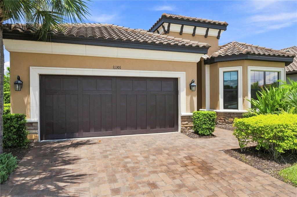 A beige house exterior features a dark brown garage door and a paved driveway — 11301 JUGLANS DRIVE, ODESSA, FL