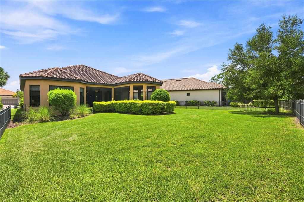 The backyard of a house features a green lawn, a screened-in patio, and landscaping — 11301 JUGLANS DRIVE, ODESSA, FL
