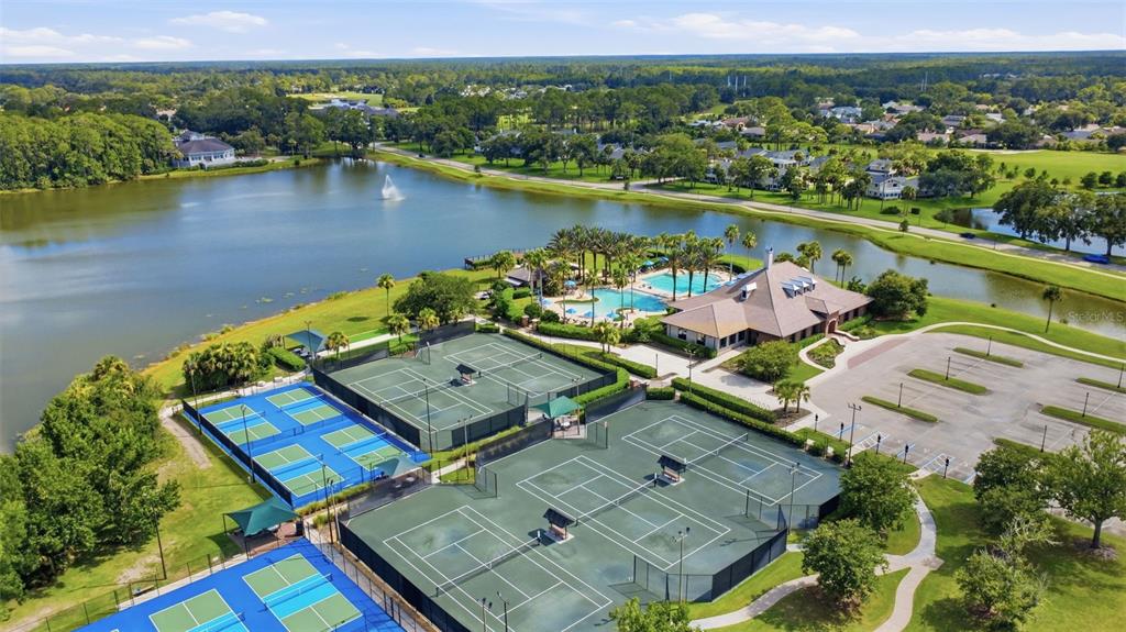An aerial view shows tennis courts, a swimming pool, and a clubhouse beside a lake — 38 TREETOP CIRCLE, ORMOND BEACH, FL