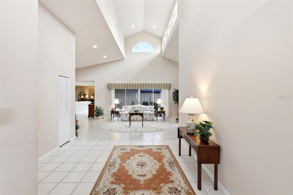 A bright, high-ceilinged living room features tile flooring, a floral sofa, and a console table — 38 TREETOP CIRCLE, ORMOND BEACH, FL