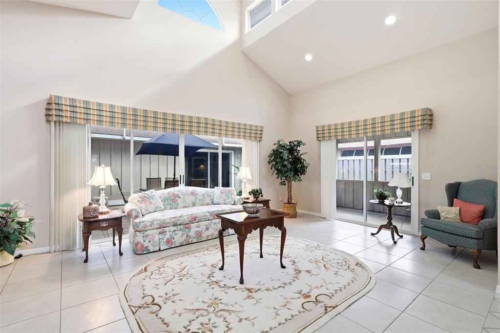 A living room with high ceilings, tile floors, a floral sofa, and sliding glass doors — 38 TREETOP CIRCLE, ORMOND BEACH, FL