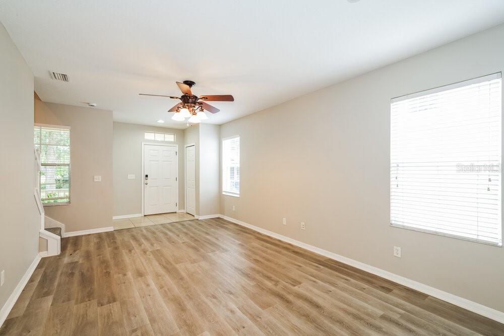 An empty room with light wood-look flooring, beige walls, a ceiling fan, and large windows — 16014 LONEOAK VIEW DRIVE, LITHIA, FL