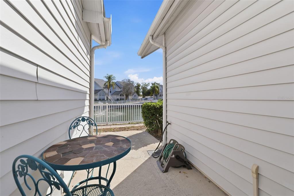 A small concrete patio sits between two white vinyl-sided walls overlooking a pond — 12245 ARMENIA GABLES CIRCLE UNIT 12245, TAMPA, FL