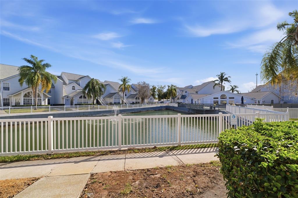A white fence borders a small pond in front of multi-story residential apartment buildings — 12245 ARMENIA GABLES CIRCLE UNIT 12245, TAMPA, FL