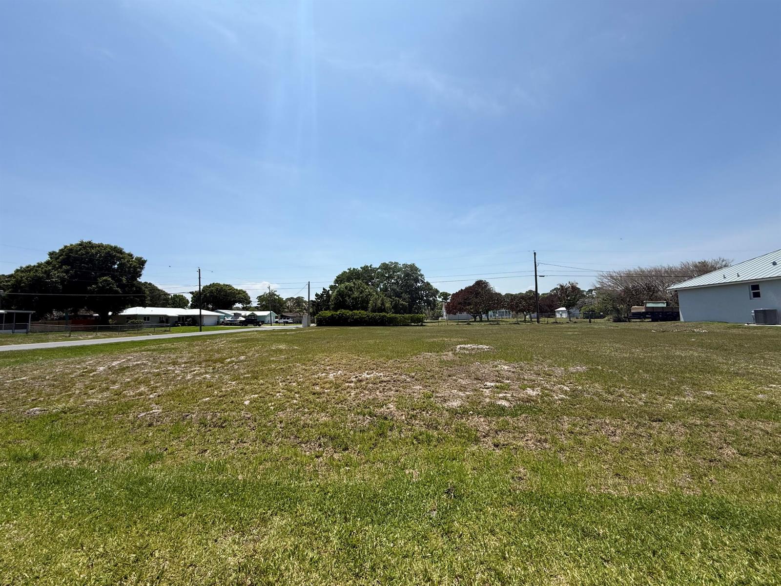 A wide, grassy vacant lot under a clear blue sky with neighboring houses nearby — Tbd Seagrape Drive, Fort Pierce FL 34982, FORT PIERCE, FL