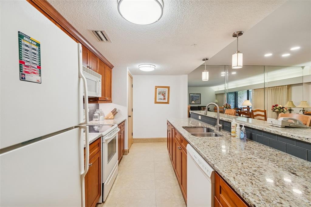 A kitchen with wood cabinets, granite countertops, white appliances, and a mirrored backsplash — 36750 US HIGHWAY 19 N UNIT 17208, PALM HARBOR, FL