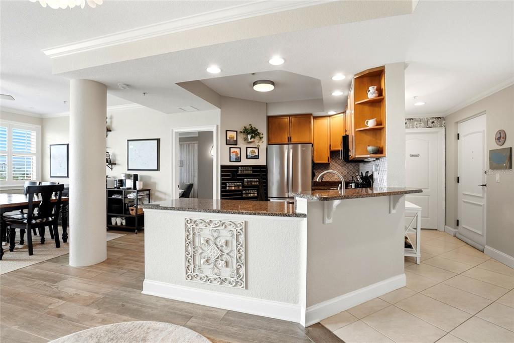A kitchen with wood cabinets and a granite-topped breakfast bar overlooks a dining area — 750 4TH AVENUE S UNIT 705D, ST PETERSBURG, FL