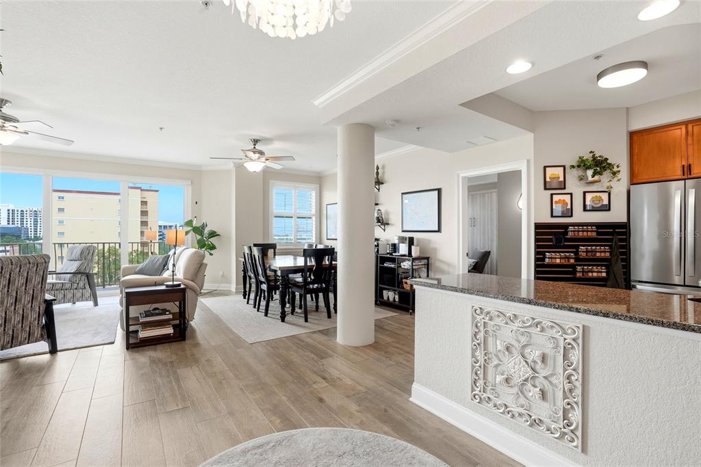 An open-concept living and dining area features wood-look flooring, a kitchen island, and balcony views — 750 4TH AVENUE S UNIT 705D, ST PETERSBURG, FL