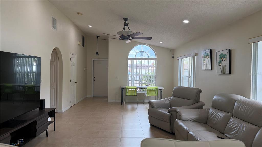 A living room with tile floors, a ceiling fan, a large window, and light-colored furniture — 632 DHARMA CIRCLE, WINTER GARDEN, FL