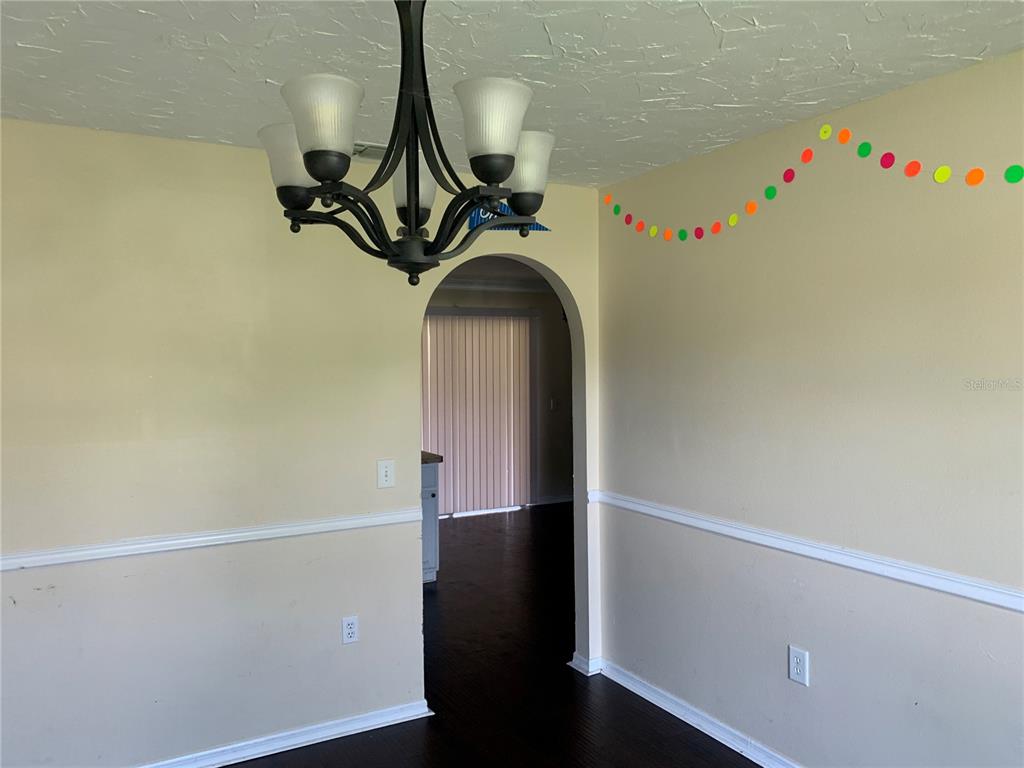 A dining room features a dark chandelier, arched doorway, chair rail molding, and dark flooring — 4300 IVEYGLEN AVENUE, ORLANDO, FL