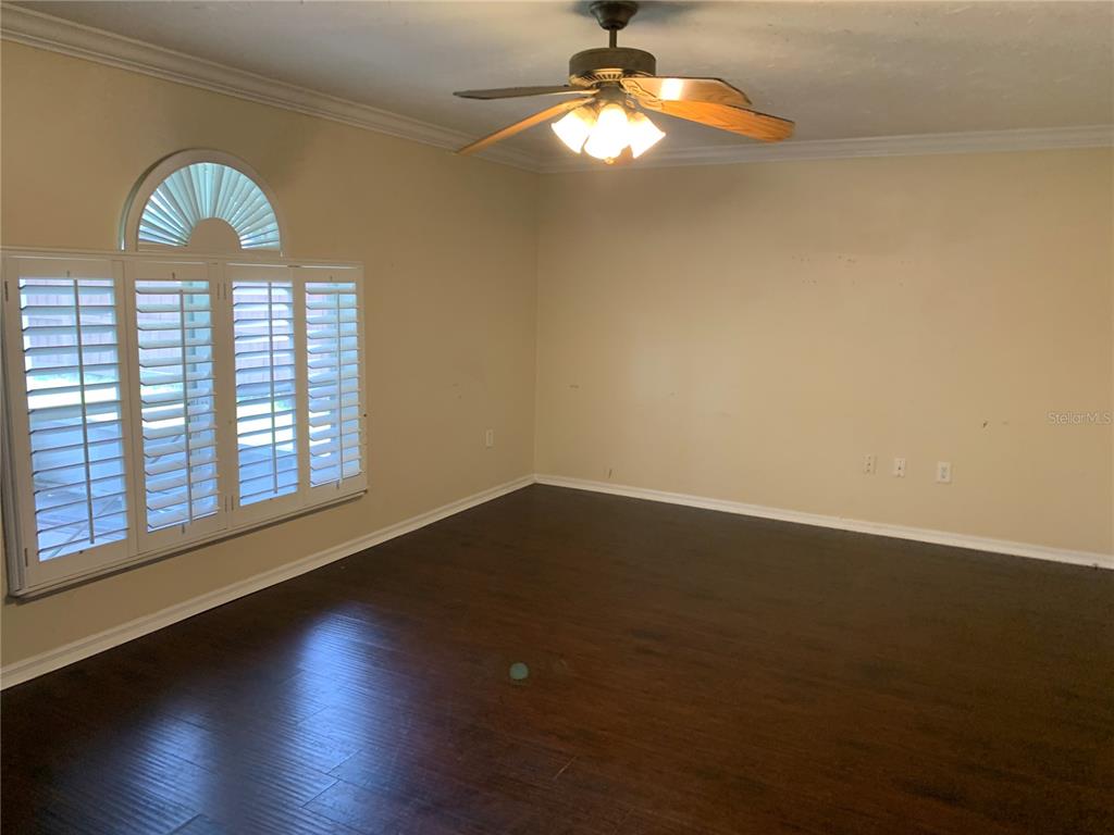 An empty room with dark wood flooring, beige walls, a ceiling fan, and shuttered windows — 4300 IVEYGLEN AVENUE, ORLANDO, FL