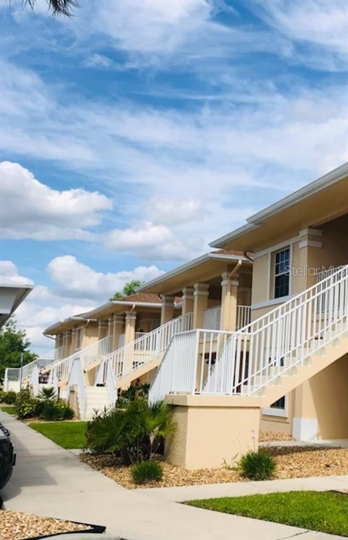 Exterior view of a multi-story apartment complex with tan stucco walls and white staircases — 26397 NADIR ROAD UNIT 204, PUNTA GORDA, FL
