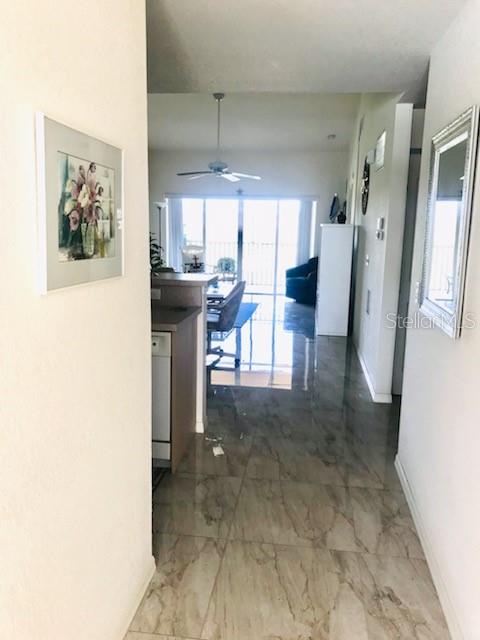 A hallway with marble-look tile flooring leads to a bright living area with a ceiling fan — 26397 NADIR ROAD UNIT 204, PUNTA GORDA, FL