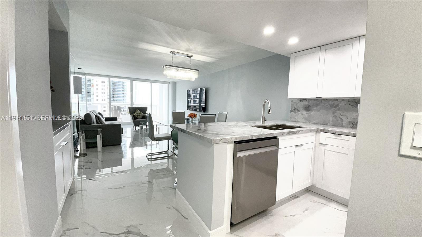 A modern kitchen with white cabinets and marble countertops opens into a living area — 1717 N Bayshore Dr # 1950, Miami FL 33132, MIAMI, FL