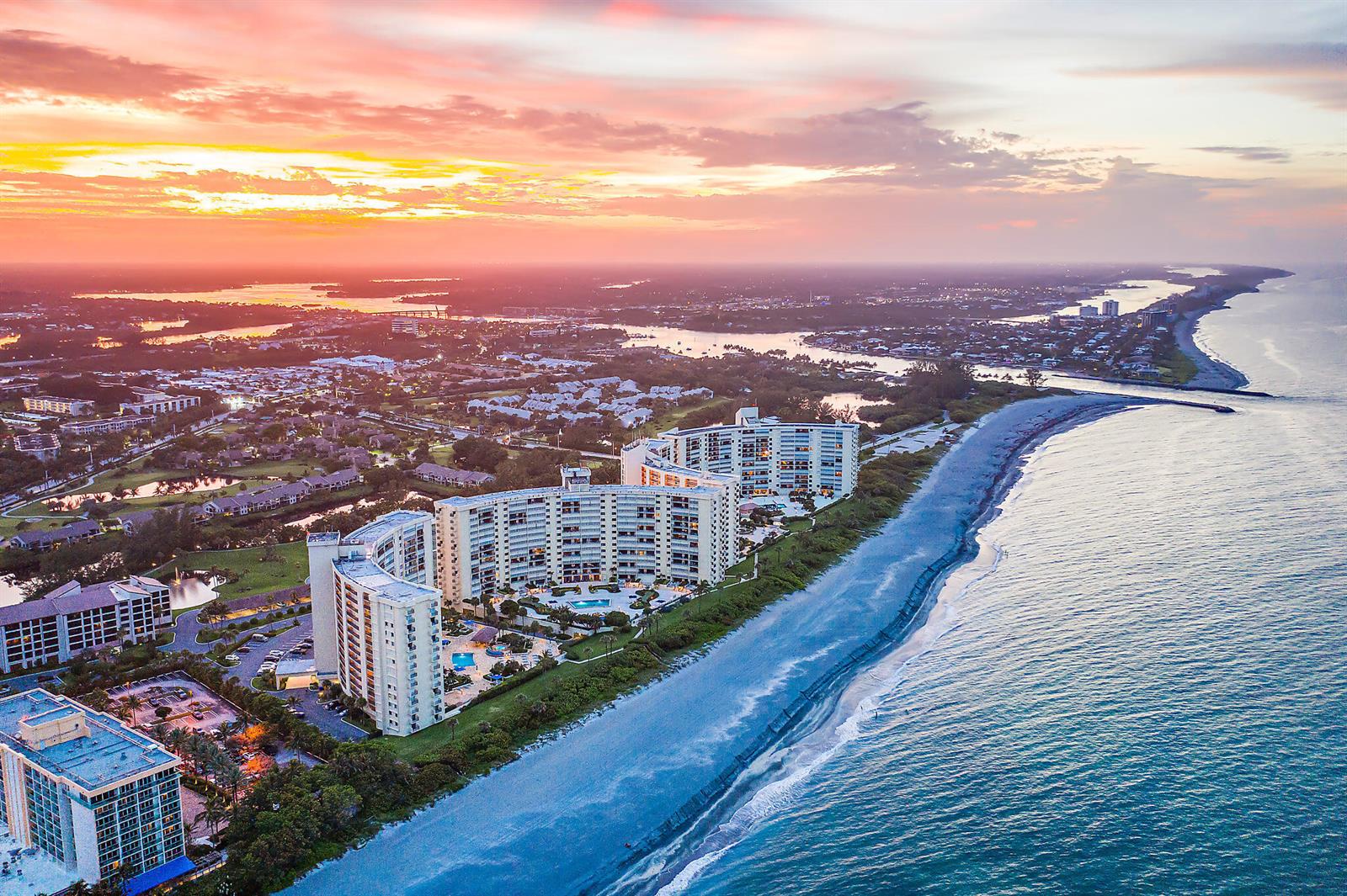 An aerial view shows high-rise beachfront condominiums along a coastline at sunset — 300 Ocean Trail Way # 403, Jupiter FL 33477, JUPITER, FL