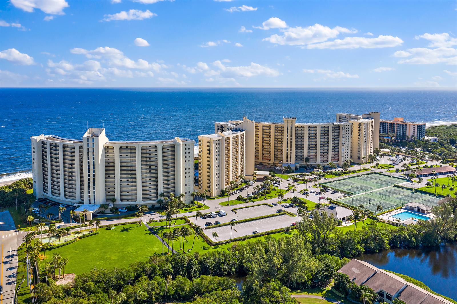 An aerial view shows a large beachfront apartment complex with tennis courts and a pool — 300 Ocean Trail Way # 403, Jupiter FL 33477, JUPITER, FL