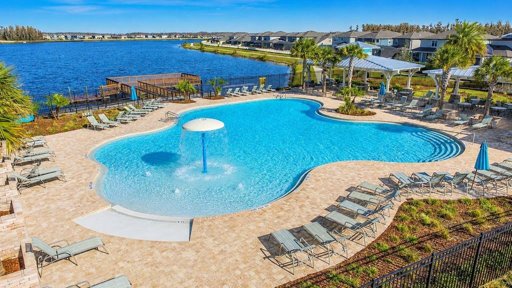 An outdoor swimming pool with a water feature sits beside a lake and patio furniture — 18843 ULMUS STREET, LUTZ, FL