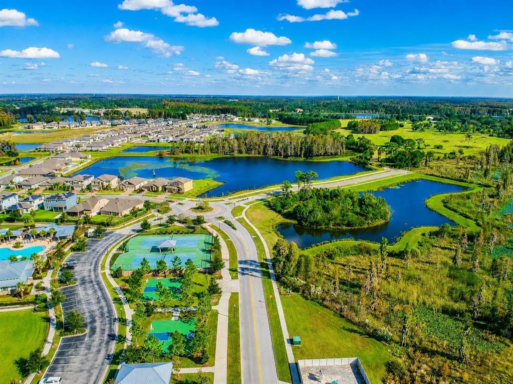 An aerial view of a suburban neighborhood featuring a lake, tennis courts, and paved roads — 18843 ULMUS STREET, LUTZ, FL