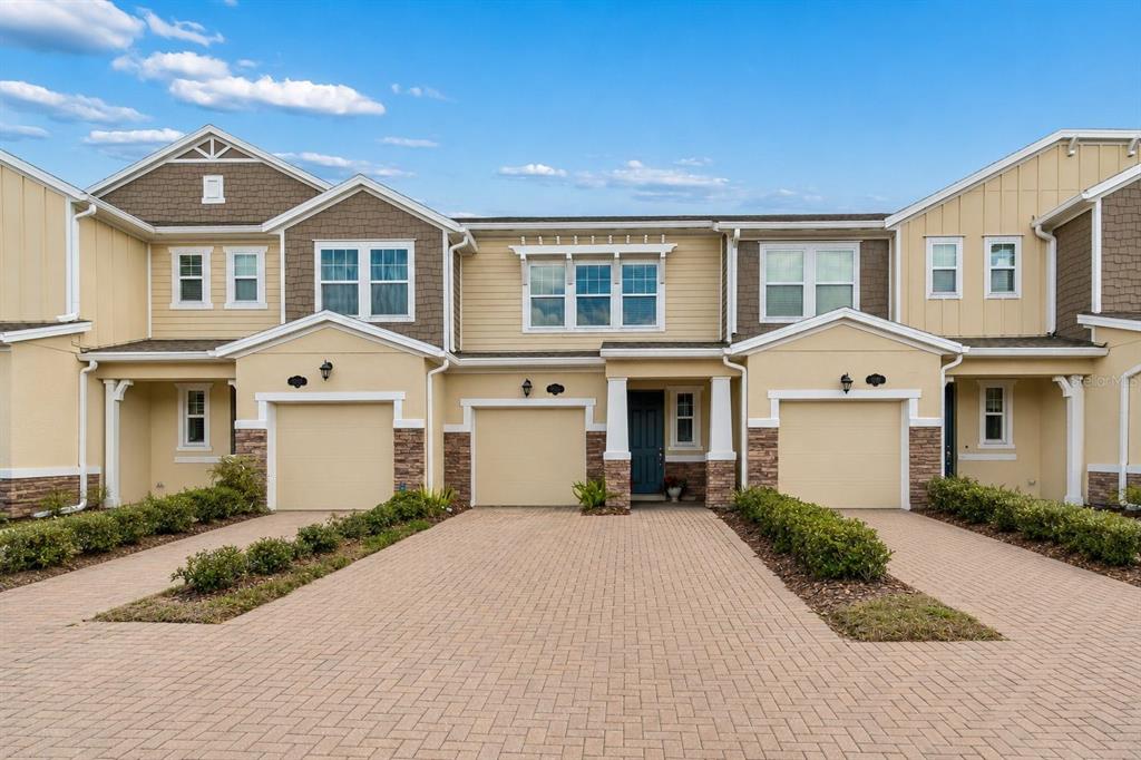 A row of three attached townhomes with tan stucco, stone accents, and paved driveways — 18843 ULMUS STREET, LUTZ, FL