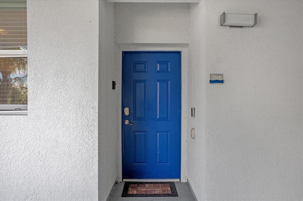 A bright blue front door with a number 204 sign on a white exterior wall — 4751 CLOCK TOWER DRIVE UNIT 204, KISSIMMEE, FL