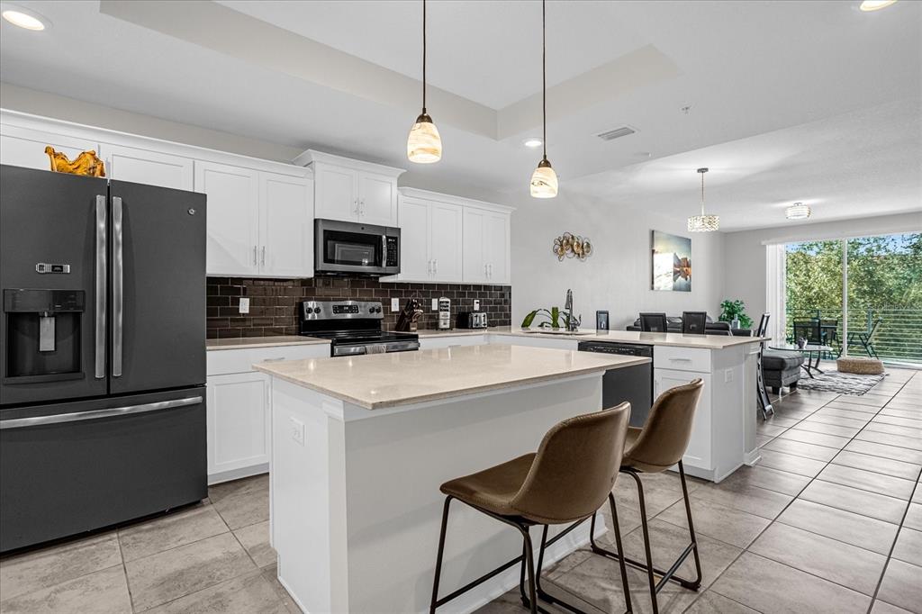 A modern kitchen features white cabinets, a central island with bar stools, and dark appliances — 4751 CLOCK TOWER DRIVE UNIT 204, KISSIMMEE, FL