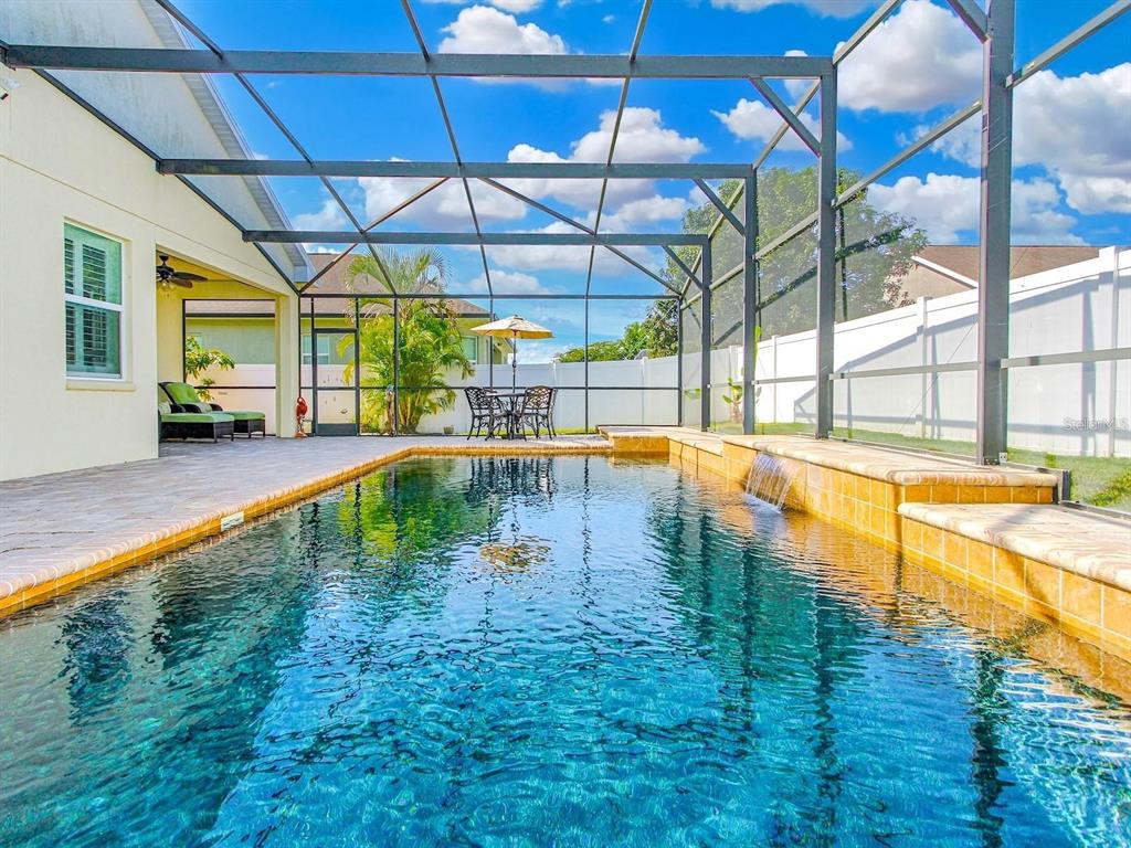 A screened-in swimming pool with a water feature and patio area under a blue sky — 4461 INDIGO SKY LANE, KISSIMMEE, FL