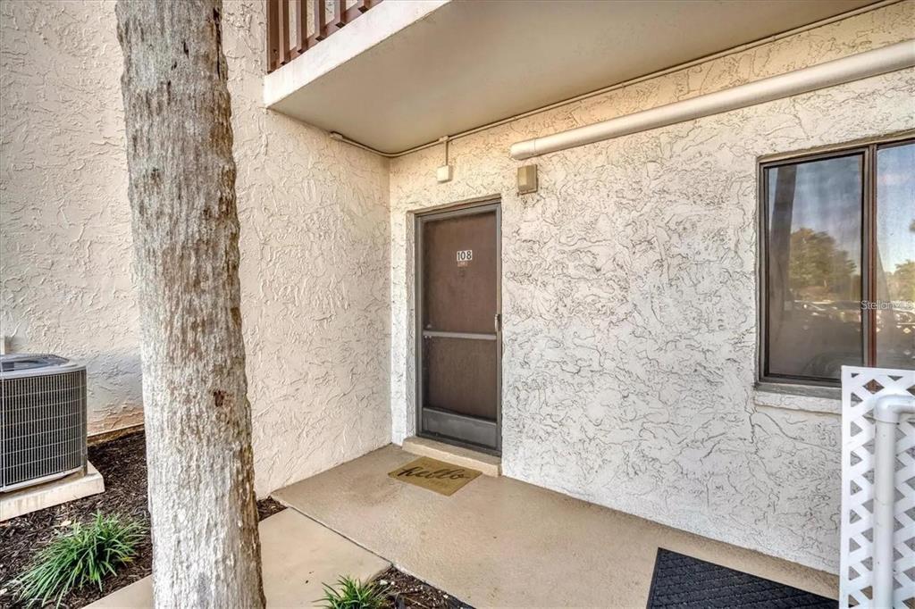 An exterior view of a ground-floor apartment entrance with a screen door and stucco walls — 1624 STICKNEY POINT ROAD UNIT 108, SARASOTA, FL
