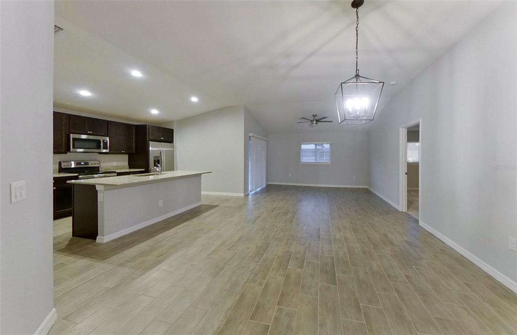 An open-concept kitchen and living area featuring dark cabinetry, a breakfast bar, and tile flooring — 227 PENNFIELD STREET, LEHIGH ACRES, FL